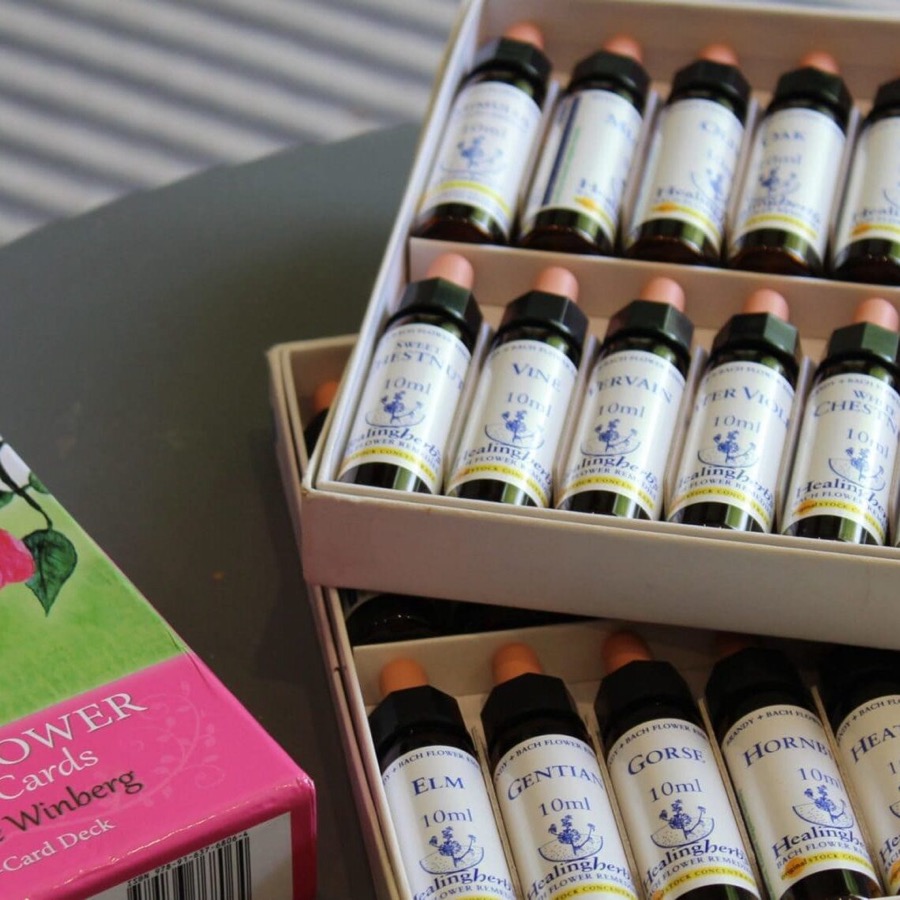 Open boxes of Healing Herbs Bach flower remedy stock bottles beside a pink Flower Cards deck on a grey table